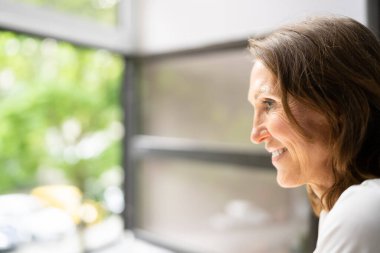 Evde pencereden bakan gülümseyen genç kadının yan görünümü