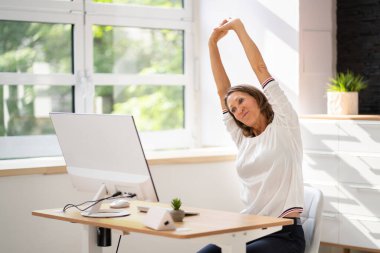 Kadın büro masasında geriniyor. Sandalye üzerinde esneme egzersizi