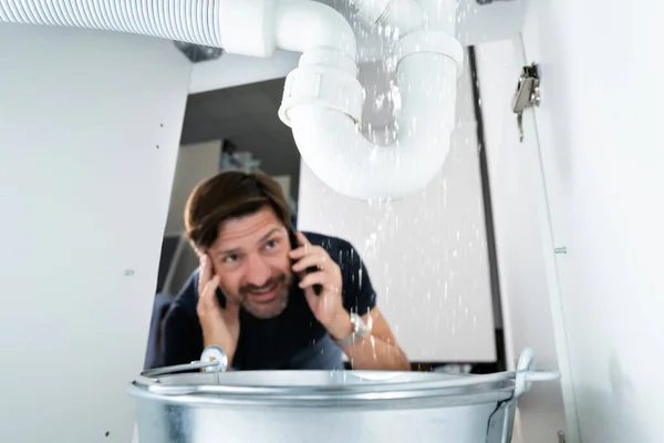 Worried Man Calling Plumber While Watching Water Leaking Sink — Fotografia de Stock