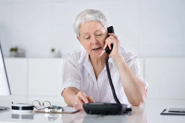Businesswoman Making A Call From Landline Phone At Desk In Office