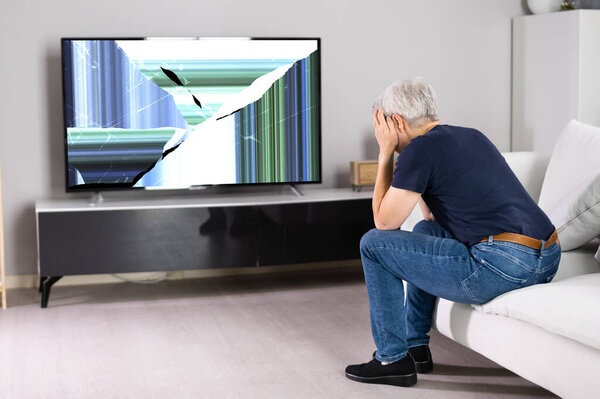 Frustrated Woman Sitting On Sofa Near Broken TV Screen