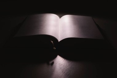 Karanlıkta beyaz masanın üzerinde açık, kalın bir kitap. 