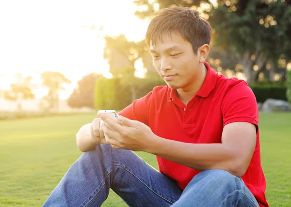 Мужчина сидит на траве и пользуется мобильным телефоном — стоковое фото