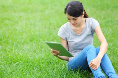 tablet bilgisayar ile çim üzerinde oturan kadın
