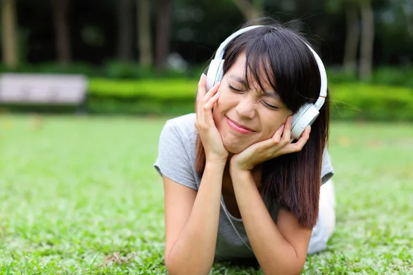 Asian woman listen to song lying on grass — Stock Photo, Image