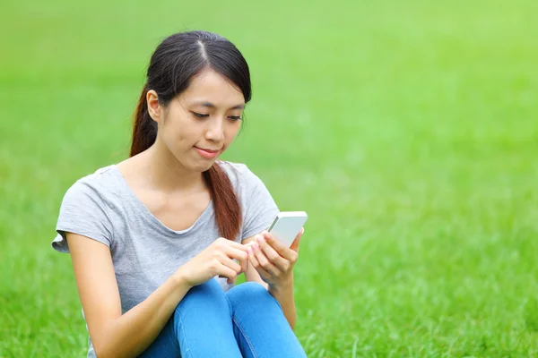 Женщина сидит на траве со смартфоном — стоковое фото