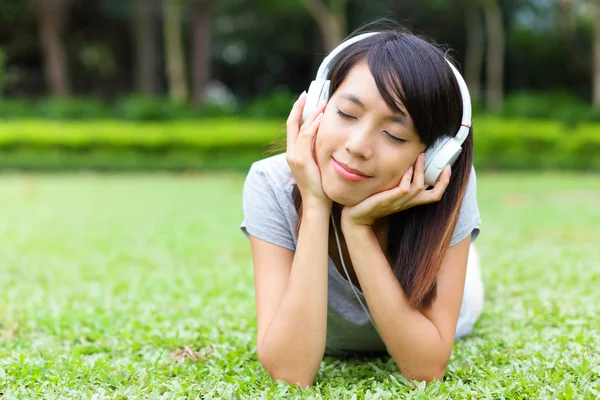 Asian woman listen to song lying on grass — Stock Photo, Image