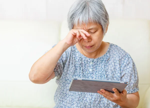 Aziatische oude vrouw met behulp van digitale tablet met vermoeide ogen — Stockfoto