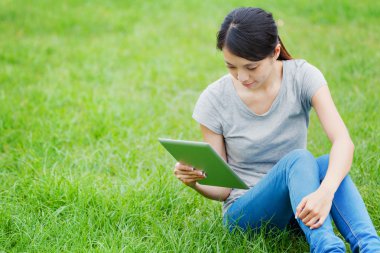 tablet bilgisayar ile çim üzerinde oturan kadın