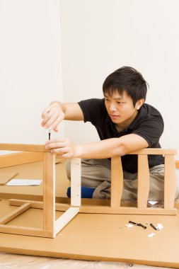 Asian man assembling chair at home clipart