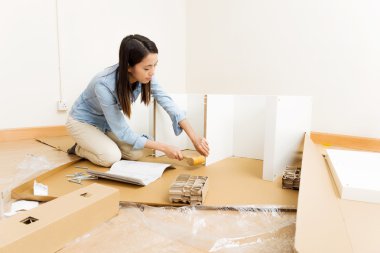 Asian woman using hammer for assembling furniture clipart