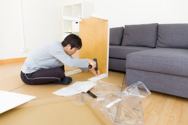 Asian man assembling table at living room clipart