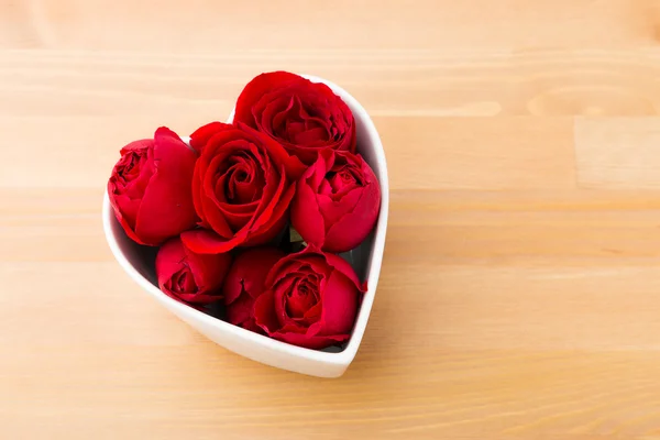 Rosa roja dentro del cuenco en forma de corazón sobre fondo de madera —  Fotos de Stock