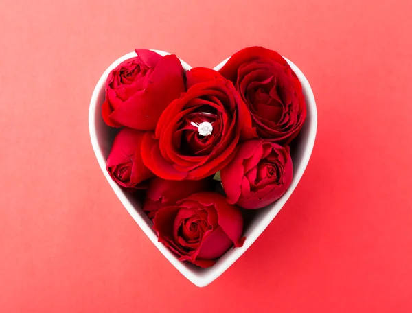 Anillo de diamantes y rosa dentro de un cuenco con forma de corazón sobre el respaldo rojo —  Fotos de Stock