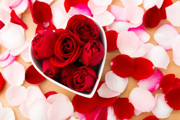 Hermosa rosa roja dentro del cuenco en forma de corazón con pétalo al lado —  Fotos de Stock