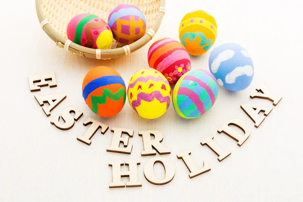 Painted easter eggs in basket with wooden text — Stock Photo, Image