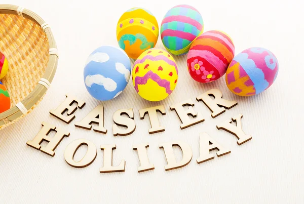 Painted easter eggs in basket with wooden text — Stock Photo, Image