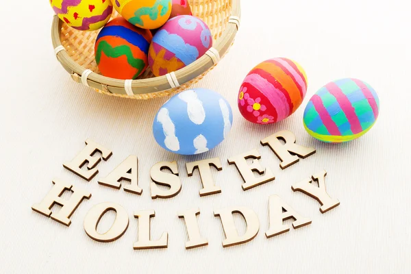 Colourful easter eggs in wicker basket with wooden text — Stock Photo, Image