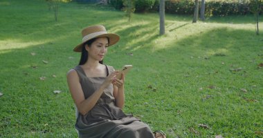 Kadın cep telefonu kullanıyor ve parkta kamp sandalyesine oturuyor.