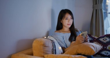 Kadın cep telefonuna bak ve evdeki kanepeye otur.