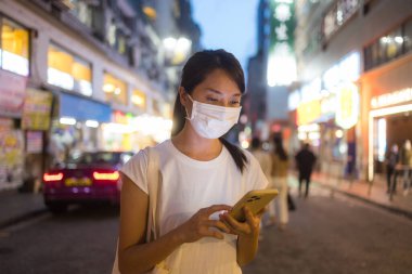 Hong Kong şehrinde kadın yüz maskesi takıyor ve cep telefonu kullanıyor.