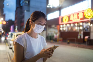 Hong Kong şehrinde kadın yüz maskesi takıyor ve cep telefonu kullanıyor.