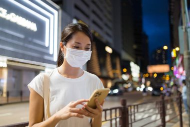 Kadın gece yüz maskesi takıyor ve cep telefonu kullanıyor.