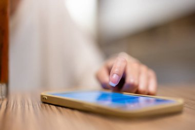 Masadaki cep telefonu ekranına dokunan kadın.