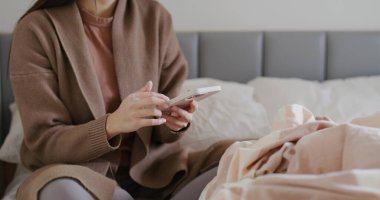 Kadın yatağında cep telefonu kullanıyor.