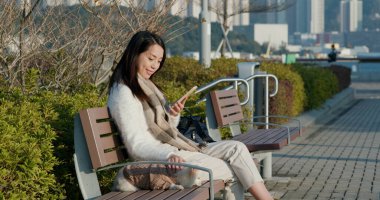 Kadın dışarıda köpeğiyle cep telefonu kullanıyor.