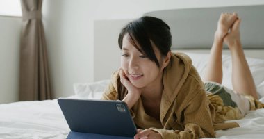 Kadın tablet bilgisayardan izliyor ve yatağa uzanıyor.