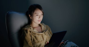 Kadın dijital tablet bilgisayarda okuyor ve geceleri sandalyeye oturuyor.