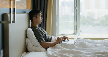Adam yatakta dizüstü bilgisayarda çalışıyor.