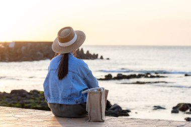 Kadın gün batımında sahilde oturur.
