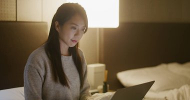 Kadın dizüstü bilgisayarda çalışır ve yatağa oturur.