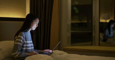 Kadın dizüstü bilgisayarda çalışır ve yatağa oturur. 