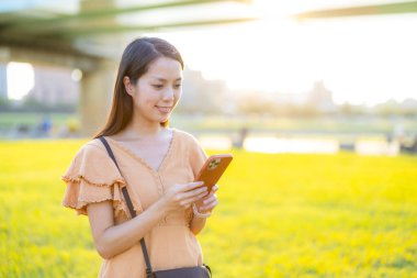 Woman use mobile phone at park under sun flare