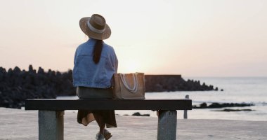 Woman sit on the bench and look at the sea at sunset