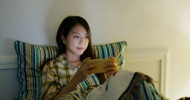 Woman play game on cellphone and lying on bed