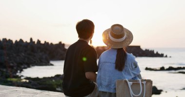 Asyalı çift gün batımında denizin kenarında oturur.