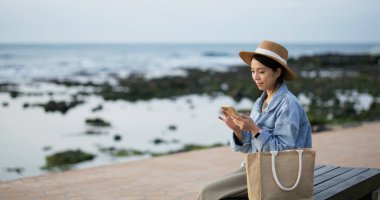 Woman use mobile phone at sit beside the sea beach
