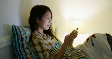 Woman play game on cellphone and lying on bed