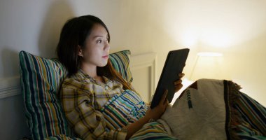 Woman read on tablet computer on bed at night