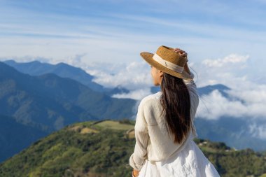Kadın terasta durur ve dağa bakar.