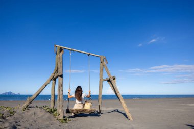Kum sahilinde salıncakta sallanan genç bir kadın.