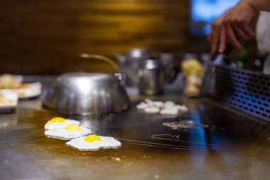 Teppanyaki şefi sıcak metal tabakta yemek hazırlıyor.