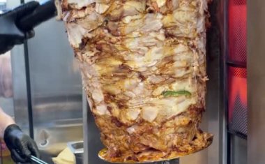 Orta sıcaklıkta ısıtılan ve shawarma (donör, jiroskop, donör kebap) için et parçaları hazırlayan dikey dönen bir şişin özel bıçağıyla eti kesmek).