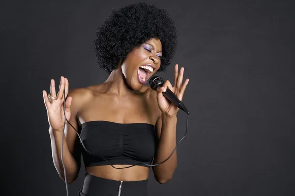 Woman singing on microphone over colored background — Stock Photo, Image