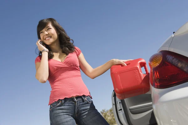 Счастливая женщина заправляет свой автомобиль, разговаривая по мобильному телефону — стоковое фото