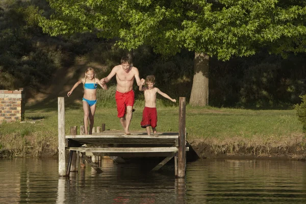 Kinderen met vader springen in lake — Stockfoto